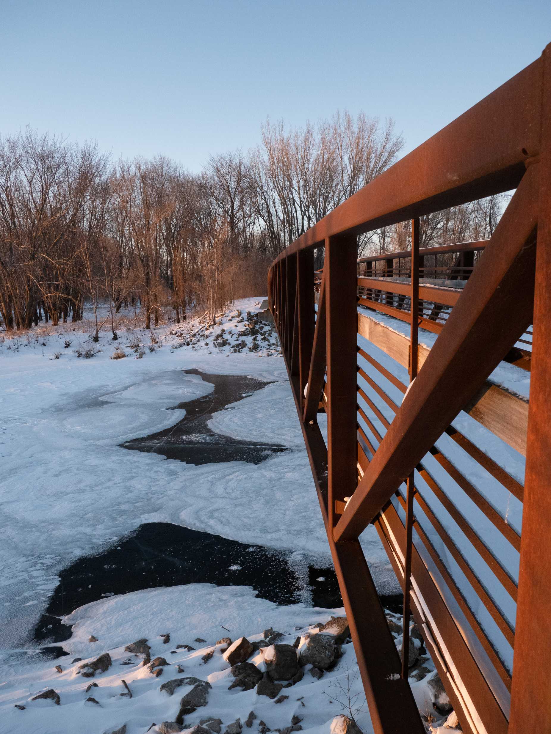 red metal bridge crossing icy water in a wooded area